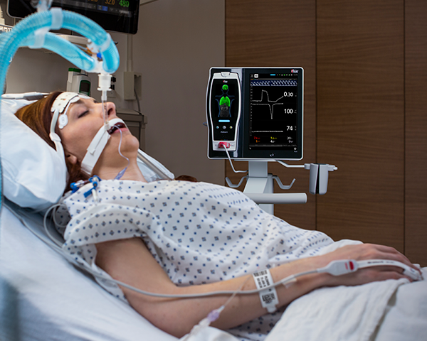 Patient endormi, intubé sur un lit d’hôpital, surveillé par un capteur du bout des doigts avec une surveillance de chevet Root et Radical-7.