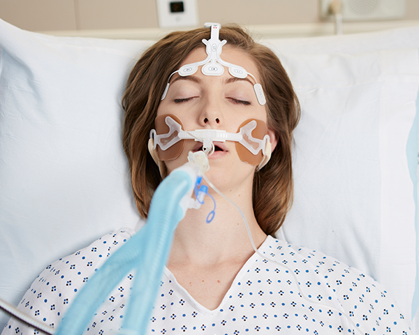 Patient endormi et intubé portant une blouse d’hôpital, surveillé par un capteur de front Masimo