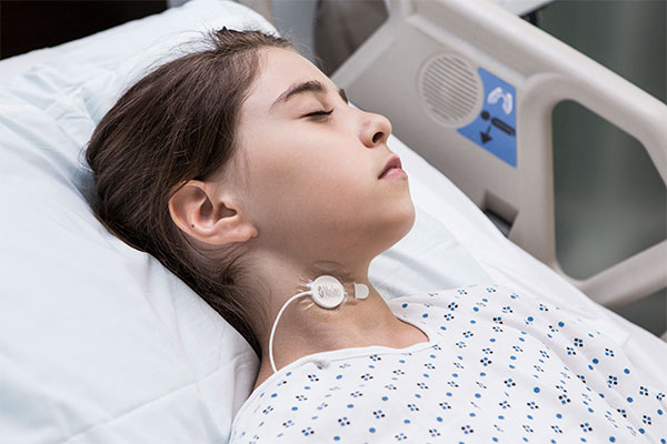 Masimo – Enfant portant un capteur de fréquence respiratoire acoustique RRa sur le cou dans un lit d'hôpital