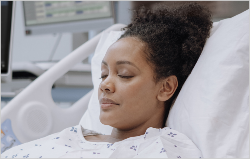 Patient à la peau foncée sur un lit d'hôpital surveillé par un dispositif Masimo Root.